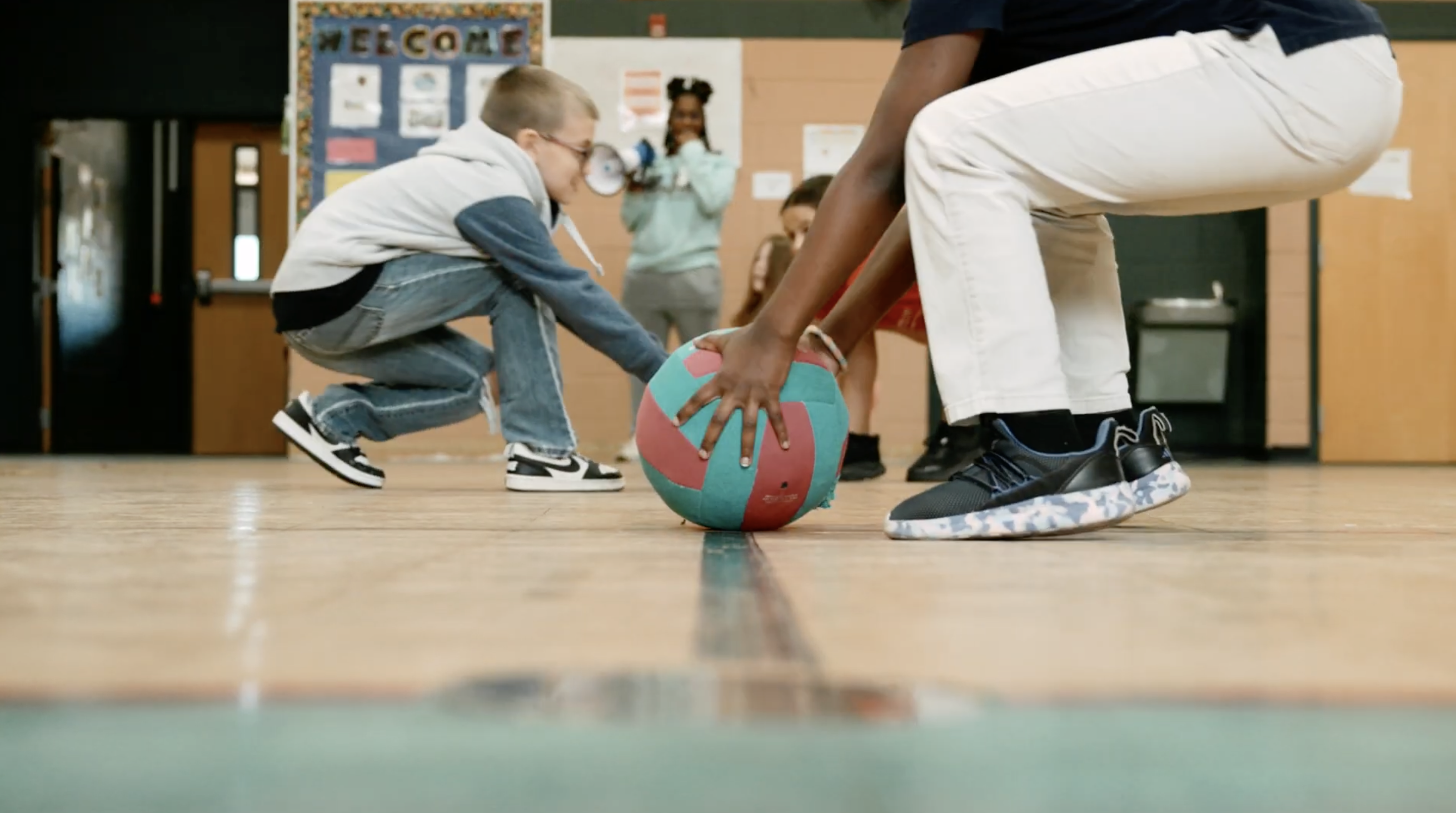 Two students bending down to grab a volleyball